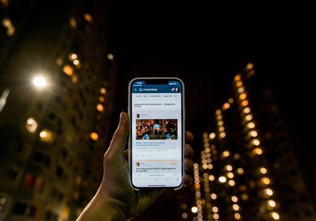 Personne tenant un smartphone affichant un article de blog en lien avec l’événementiel, sur fond de ville nocturne — illustration de la lecture de contenus digitaux sur mobile dans le secteur événementiel.